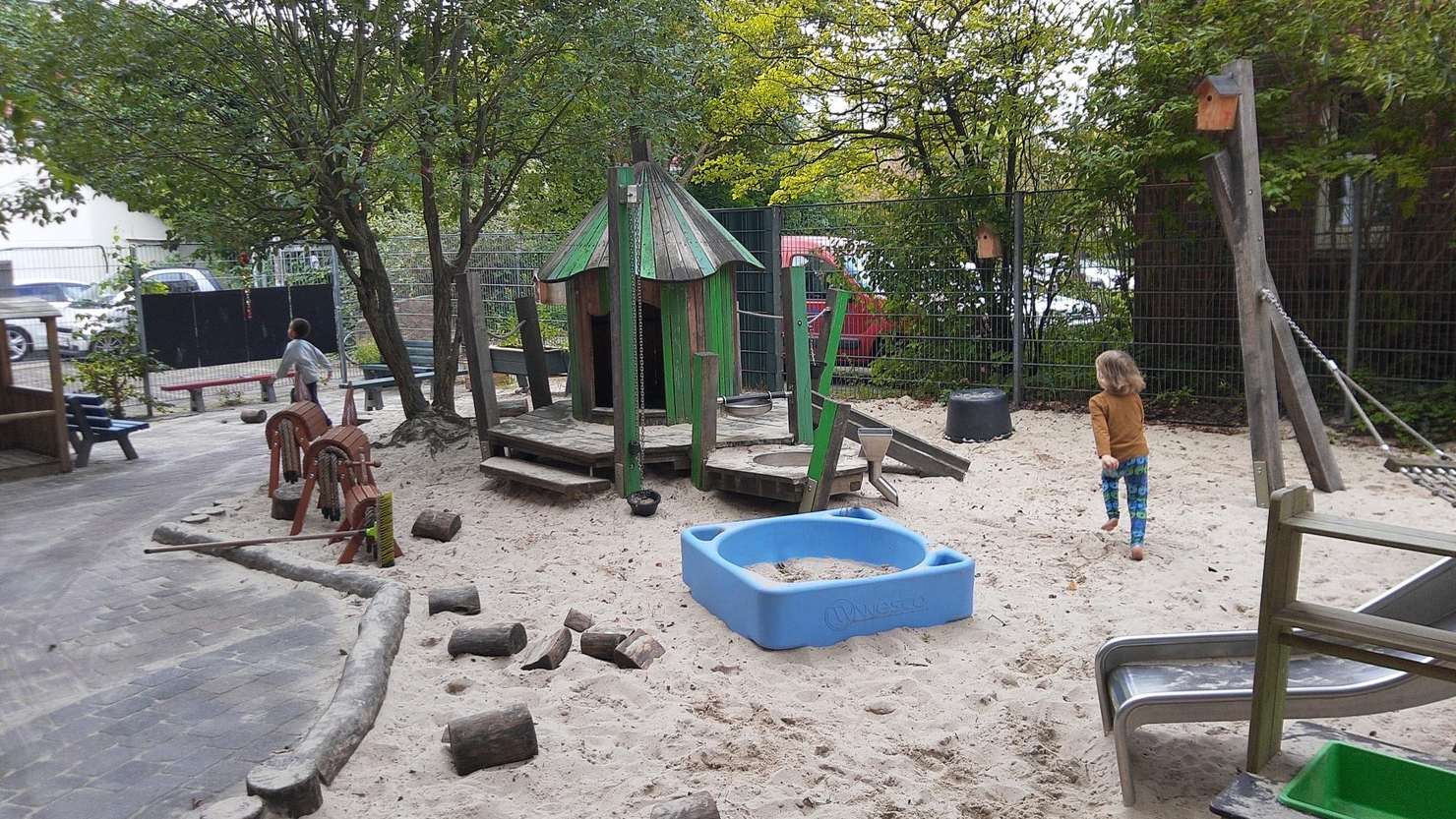 Außengelände der Freien Kita mit großem Sandkasten, Klettermikado und Gartenbereich